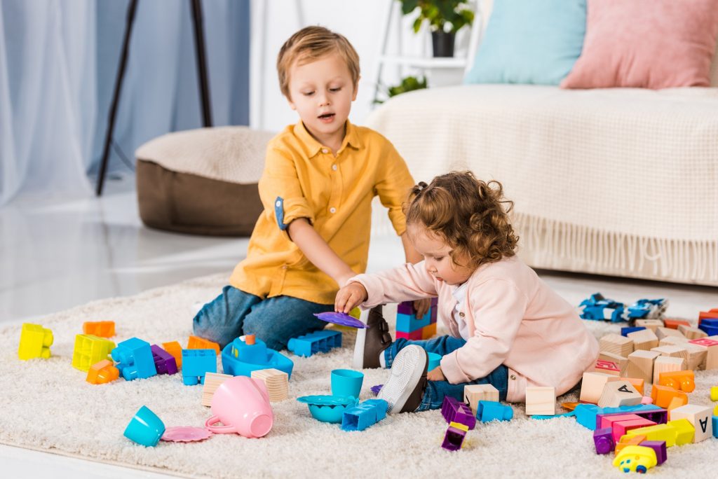 adorable siblings playing with plastic blocks on floor